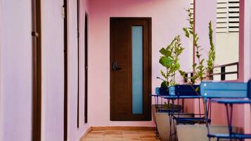A corridor with a wooden door, a tiled floor, and blue chairs arranged along the wall.