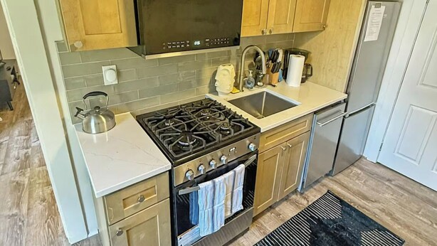 Eine Küche mit Holzausstattung, einer Edelstahl-Dunstabzugshaube, einem Gasherd, einem Backofen und einem Kühlschrank.