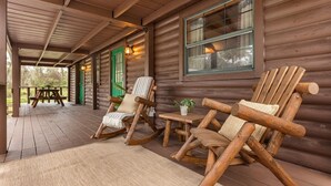 Eine Holzhütte mit einer Veranda, zwei Schaukelstühlen, einem kleinen Tisch und einer grünen Tür.