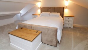 A bedroom with a bed, bedside tables, a bench, and a sloped ceiling. - Glan y Mor (Porthmadog)