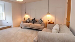 A modern living room with a beige sofa set, two pendant lights, and a small side table with a lamp. - Glan y Mor (Porthmadog)