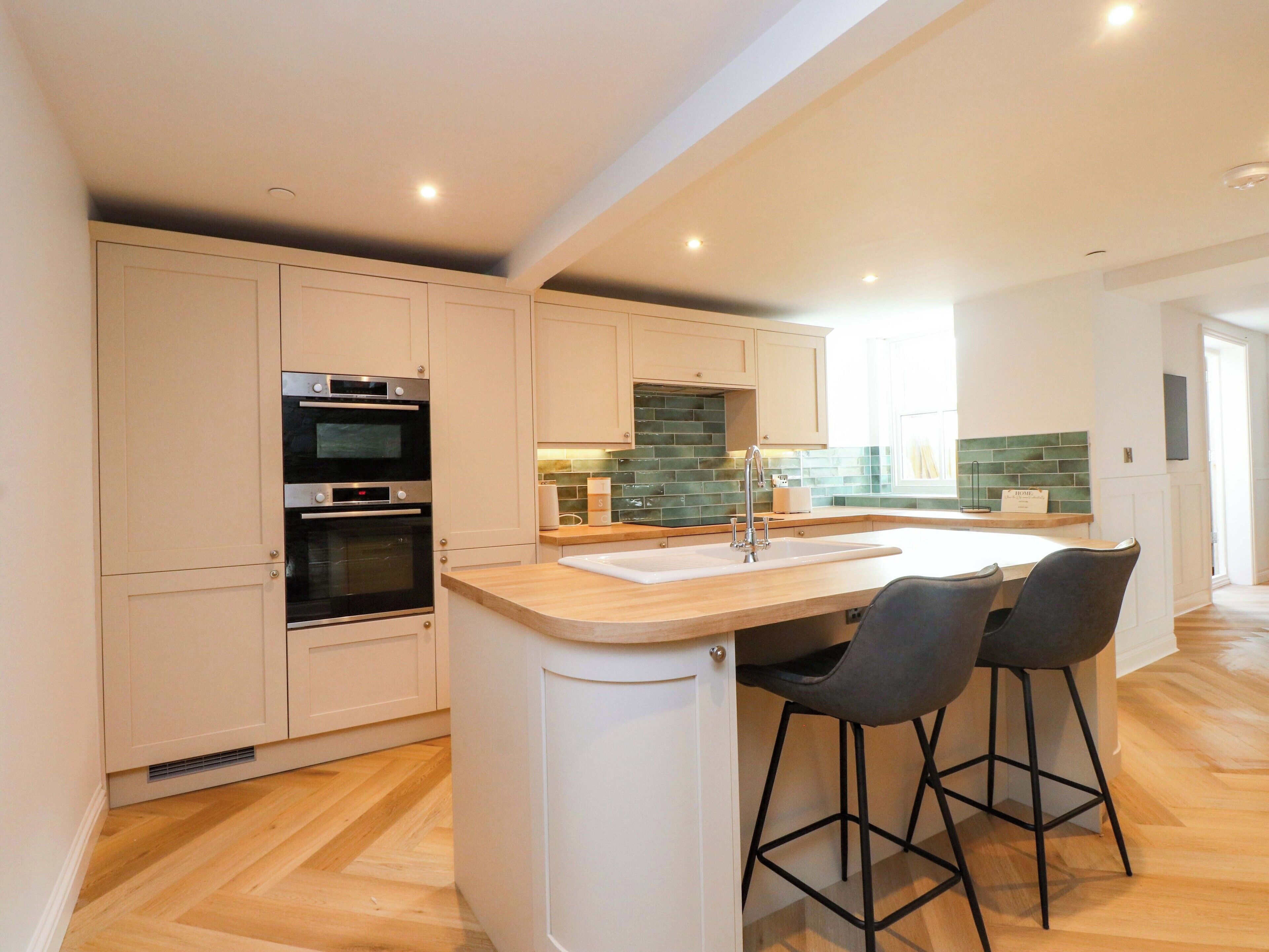 A modern kitchen with two bar stools, a built-in oven, and a large window.