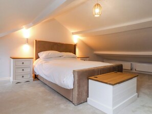 Un dormitorio con una cama grande, mesitas de noche, un banco y una lámpara colgante.