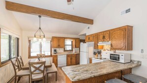 A kitchen with wooden cabinets, a marble countertop, and a dining area with wooden chairs.