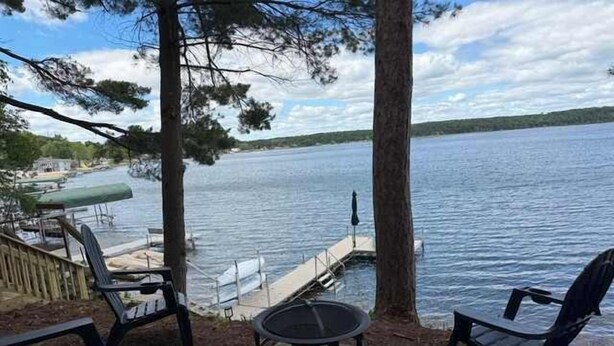 A lakeside deck with outdoor seating, a fire pit, and a dock extending into the water.