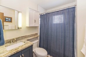 A bathroom with a marble countertop sink, a toilet, and a shower curtain.