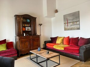 A living room with a wooden cabinet, a sofa with colorful cushions, a coffee table, and a painting on the wall.