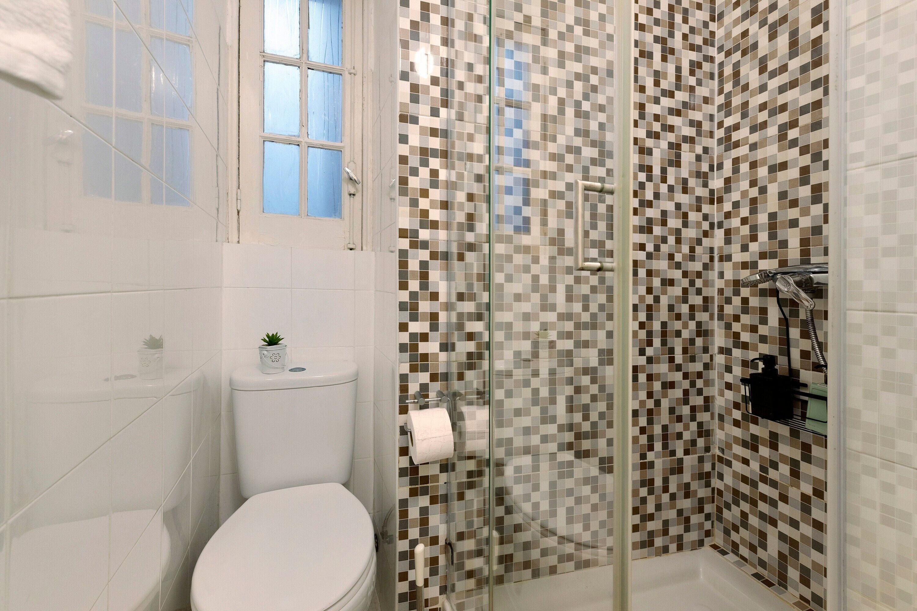 A bathroom with a toilet, a glass shower enclosure, and a checkered tile wall.
