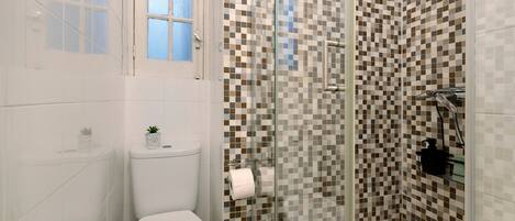 A bathroom with a toilet, a glass shower enclosure, and a checkered tile wall.