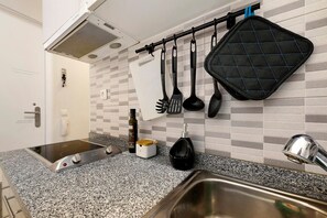 A kitchen with a granite countertop, a built-in stove, a hanging pot rack, and a black kettle. - 'São Miguel Alfama' Apartment with Balcony, Wi-Fi and Air Conditioning (Lisbon)