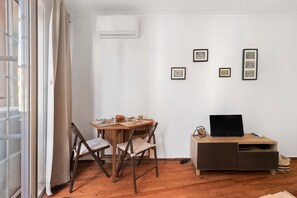 A room with a wooden dining table, two chairs, a TV on a wooden cabinet, and framed pictures on the wall. - 'São Miguel Alfama' Apartment with Balcony, Wi-Fi and Air Conditioning (Lisbon)