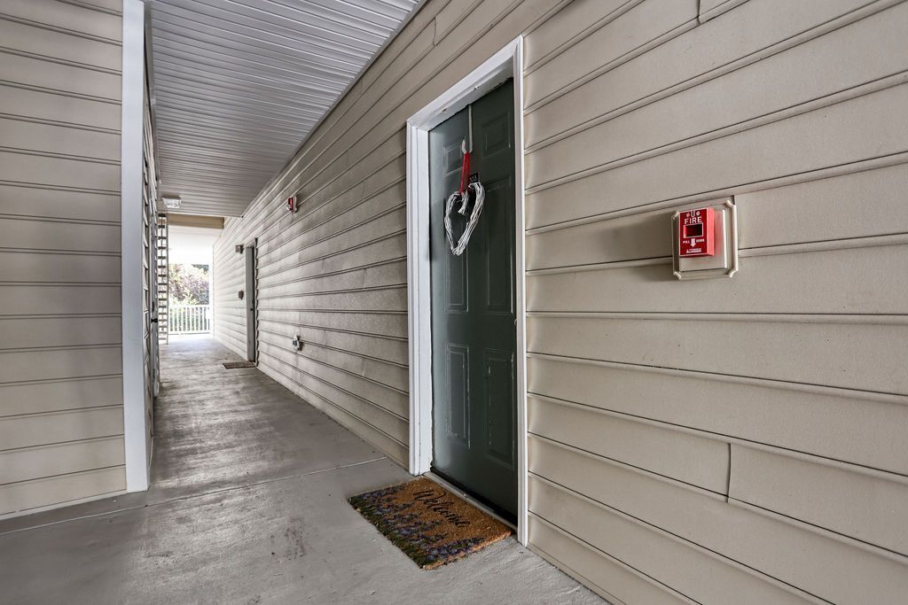 A hallway with a fire alarm and a doormat.