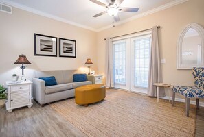 A living room with a sofa, ottoman, two lamps, a side table, a chair, and a ceiling fan. - St. Simons Island Condo | Pool, Gym & Near Beach (St. Simons Island)