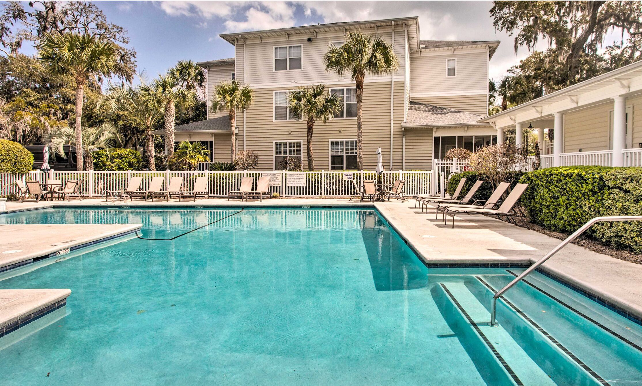A pool area with lounge chairs and a building with multiple windows and balconies.
