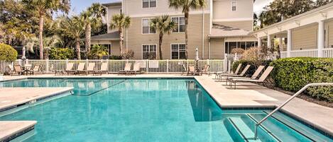 A pool area with lounge chairs and a building with multiple windows and balconies.