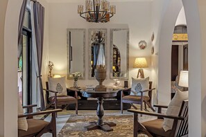 Espaço de jantar formal com mesa redonda, cadeiras e um candelabro.