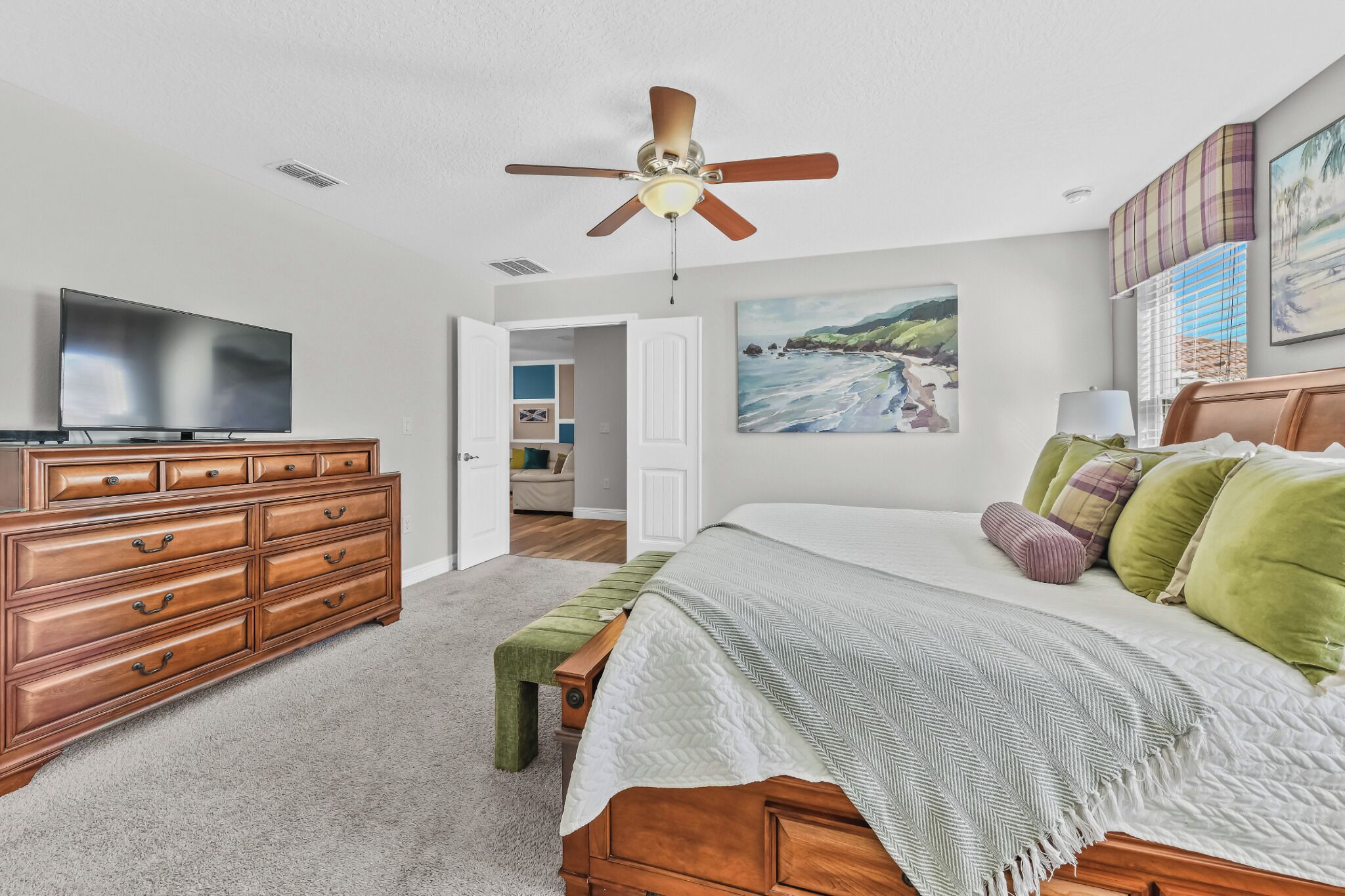A bedroom with a bed, a dresser, a television, and a ceiling fan.