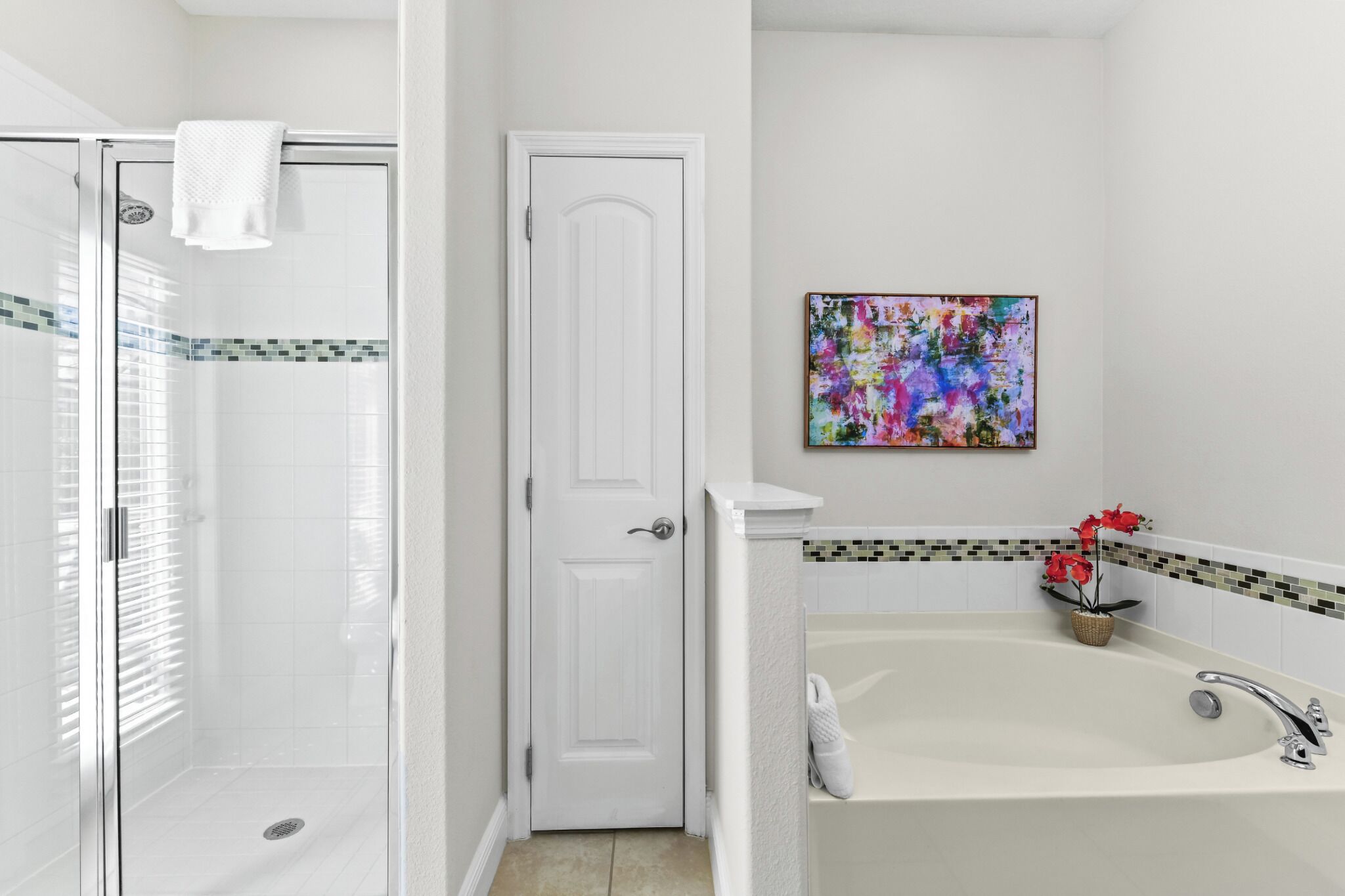 Un baño con ducha, bañera, una puerta y un cuadro abstracto y colorido en la pared.