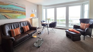 Ett modernt hotellrum med en soffa i läder, ett soffbord i glas, ett matbord med stolar och stora fönster med utsikt över omgivningarna.