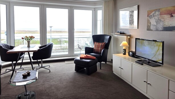 Ett modernt hotellrum med ett stort fönster, en platt-TV, en bekväm sittgrupp och ett litet bord med en vas med blommor.
