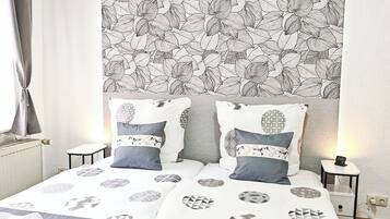 A neatly made bed with patterned bedding, a headboard with a leaf pattern, and a bedside table with a lamp.