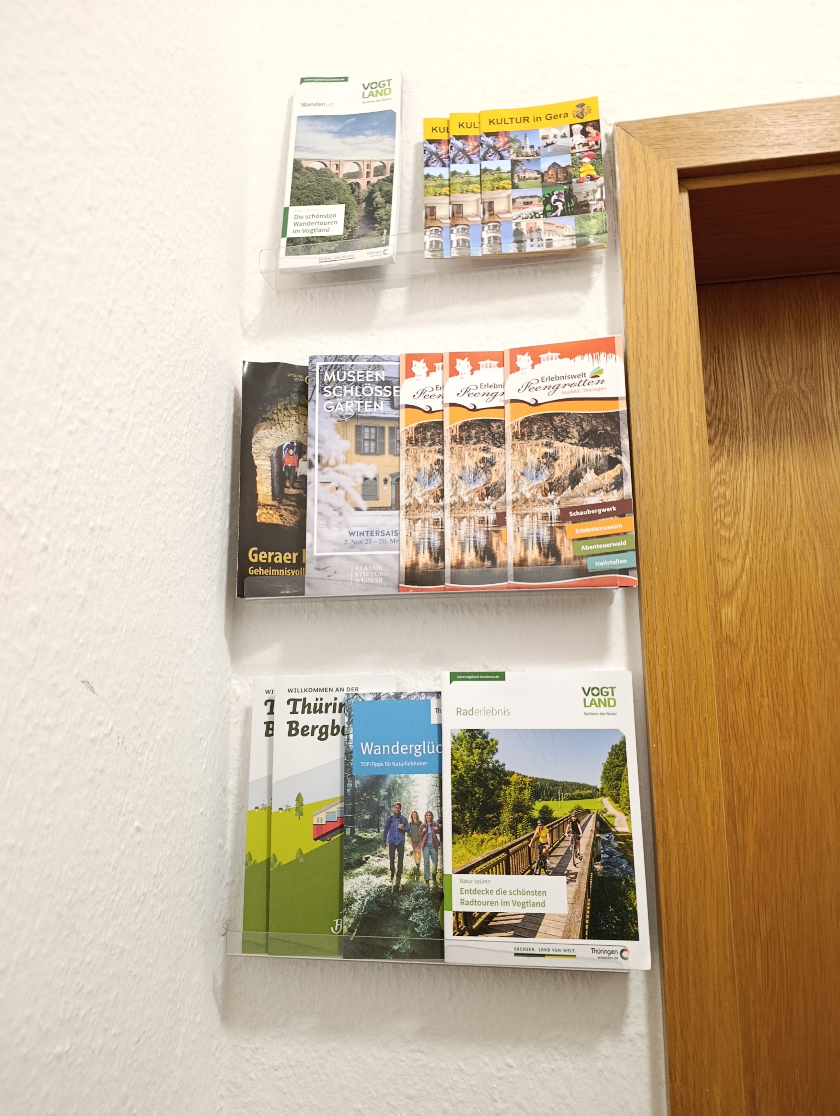 Een muur met brochures voor de Vogtland en Thüringen regio's, inclusief reistips en lokale bezienswaardigheden.
