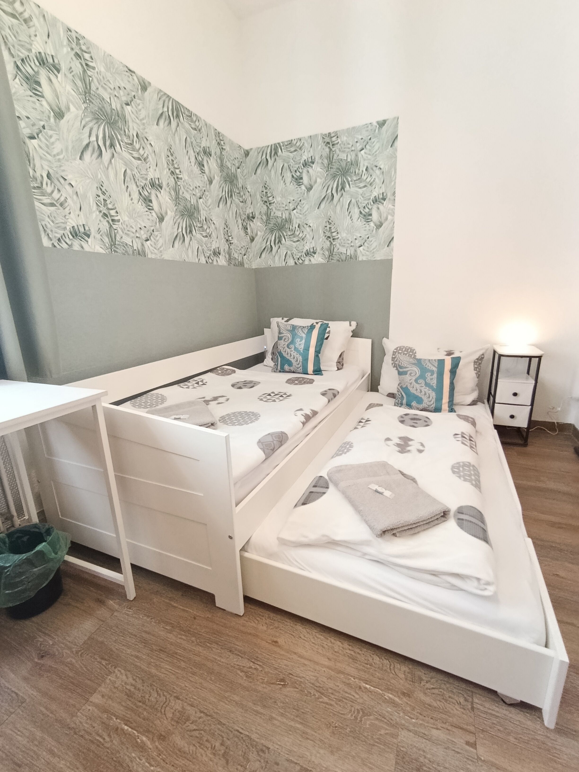 A corner bedroom with a bed, a desk, and a nightstand.
