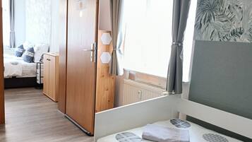 A bedroom with a bed, wooden wardrobe, and a view of another room.