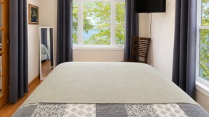 Een slaapkamer met een bed, een televisie, een raam met gordijnen en uitzicht op groen.