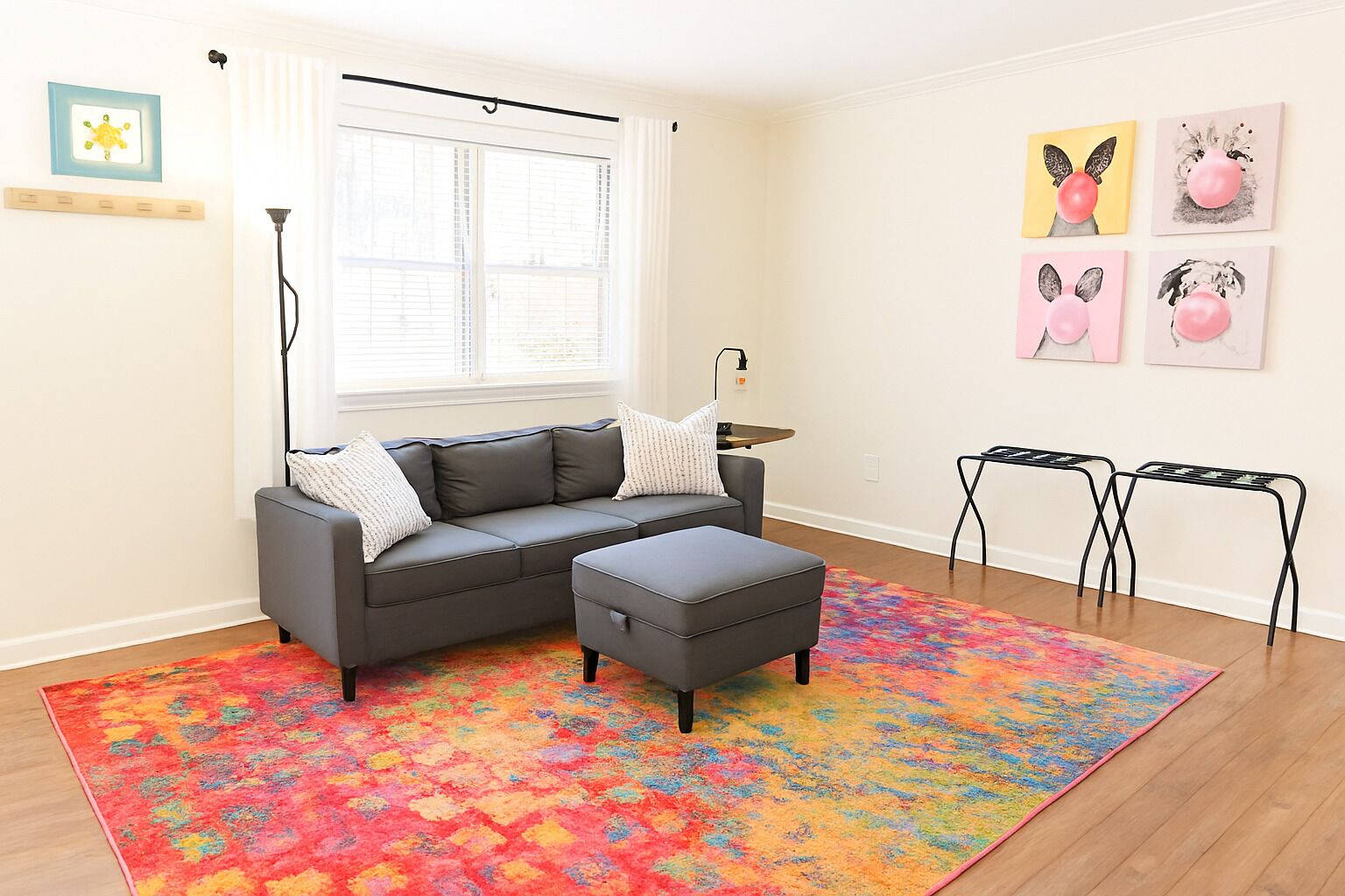 Una sala de estar moderna con un sofá seccional gris, un reposapiés, una alfombra colorida, una mesita y obras de arte en la pared.