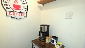 Una cucina compatta con macchina per il caffè, un piccolo tavolo e uno scaffale sopra con contenitori per il caffè.