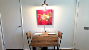 Un'area pranzo con un tavolo in legno, quattro sedie, un quadro astratto rosso e una lampada a sospensione.