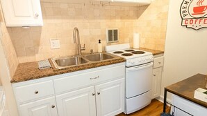 Cucina con pensili bianchi, piano di lavoro in granito, fornello e lavello.