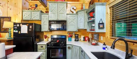 A compact kitchen with wooden cabinets, a black refrigerator, a stove, and a microwave.