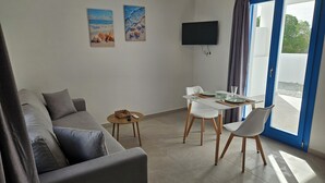Un soggiorno moderno con un divano grigio, un tavolino rotondo con un vassoio, un tavolo da pranzo con sedie e una TV a parete.
