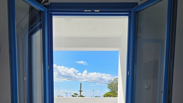 Zona pranzo con tavolo apparecchiato per due, con vista sul cielo e sulle nuvole attraverso porte blu a cornice aperta.