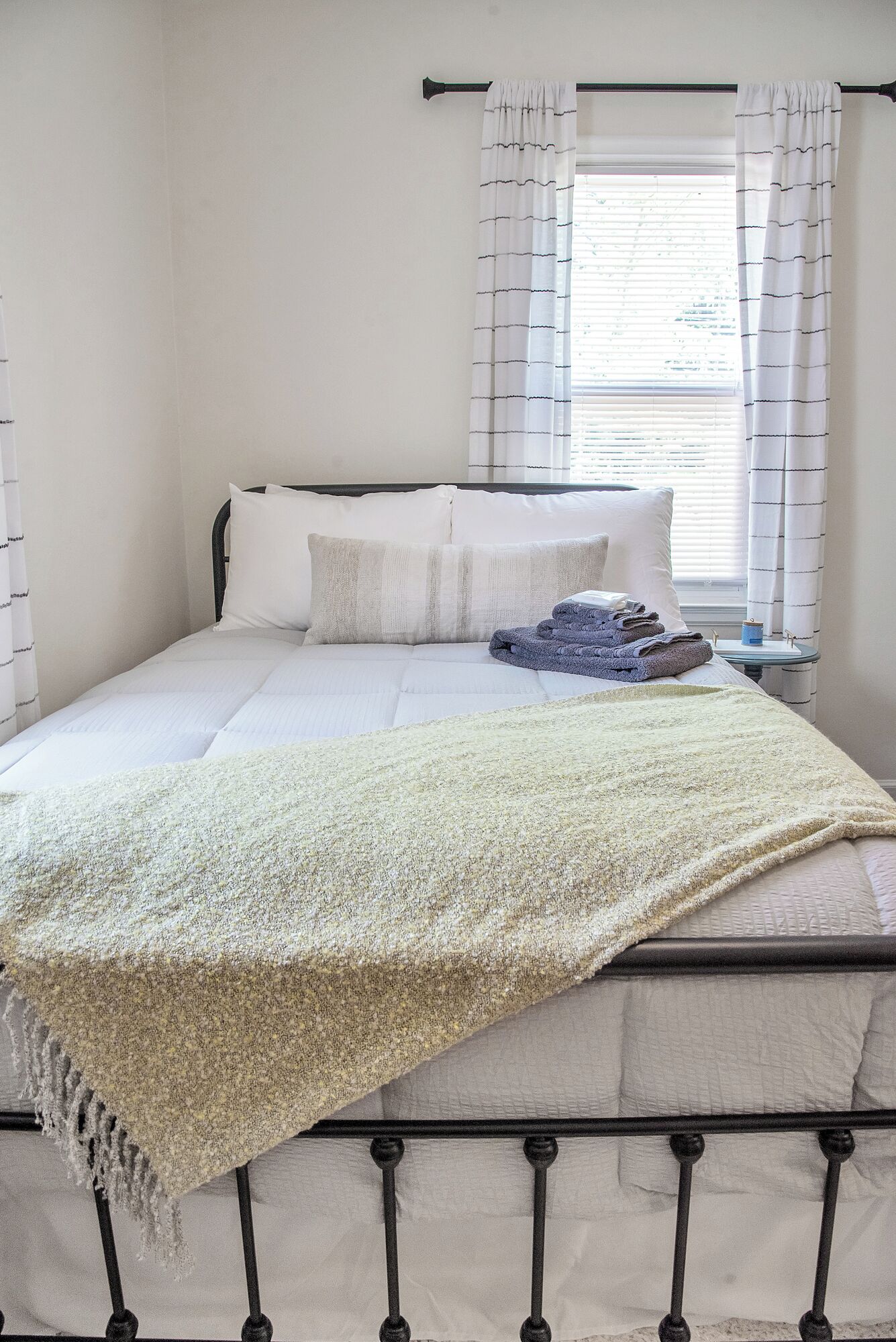 A neatly made bed with a white comforter and pillows, a folded blanket on the side, and a small table with a lamp and a book.