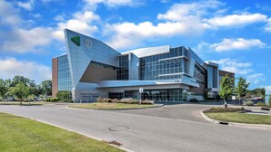 Un edificio moderno con facciata in vetro curvo e un logo verde ben visibile, con l'indirizzo 