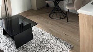 A modern living room with a round dining table, a flat-screen TV mounted on the wall, a round mirror, and a glass coffee table. - Renovated studio with wifi-center of town and beach on foot (Cabourg)