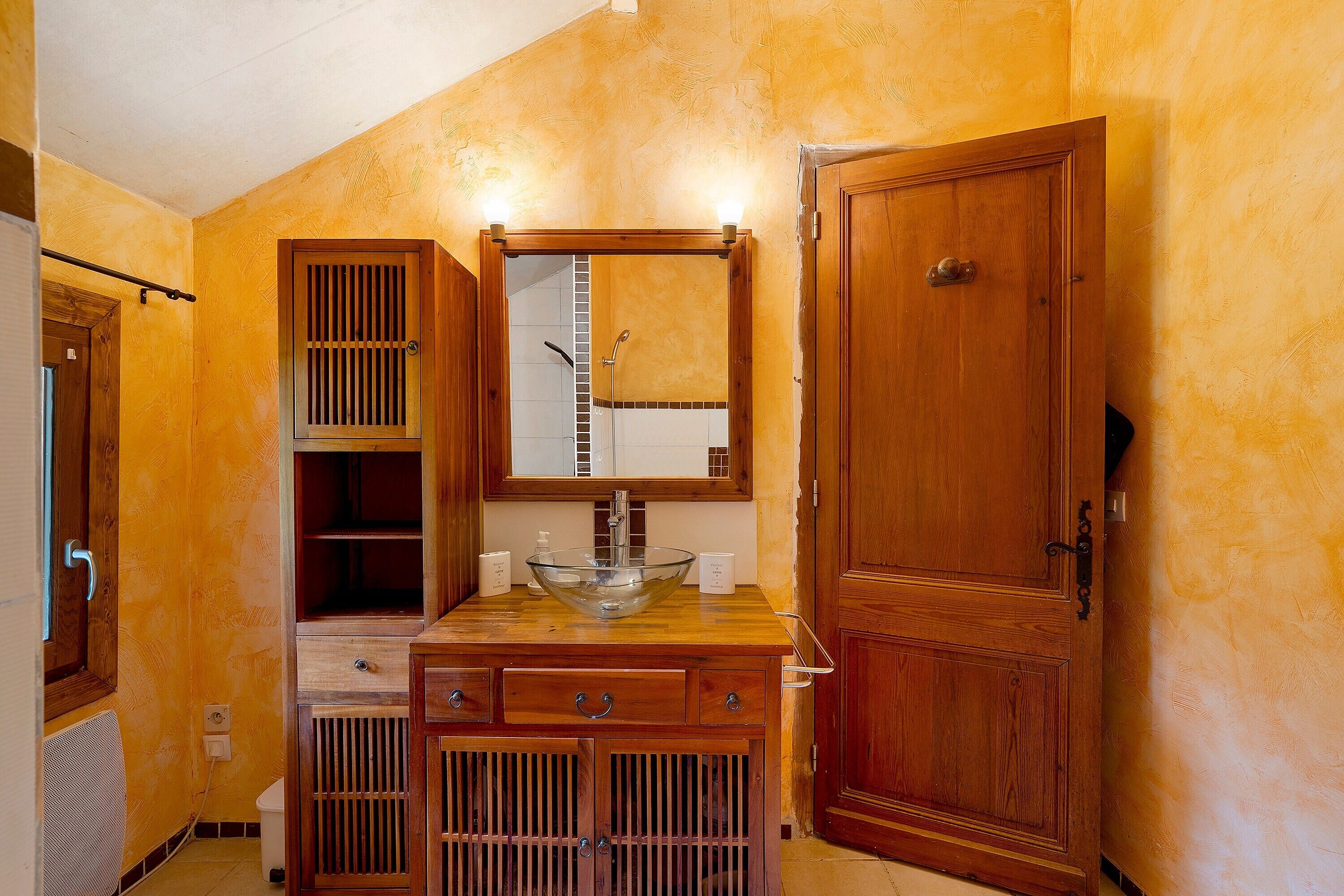 A bathroom with a wooden vanity, a glass bowl sink, a mirror, and a door.