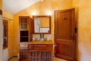 A bathroom with a wooden vanity, a glass bowl sink, a mirror, and a door.