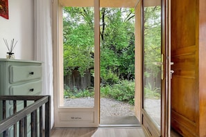 Una habitación con puerta de vidrio corredera que da a un jardín, piso de madera y cómoda de color claro.