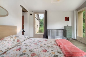 Un dormitorio con una cama, una cuna, un aparador y una ventana con vistas.