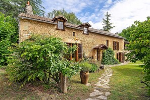 A stone house with a garden path, wooden shutters, and a stone chimney.