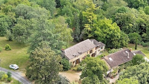 A two-story house surrounded by dense greenery, with a visible driveway and a parked car.