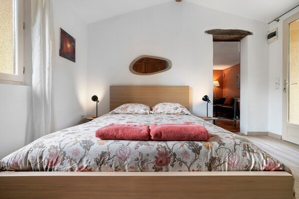 A bedroom with a wooden bed, floral bedding, and a nightstand with a lamp.