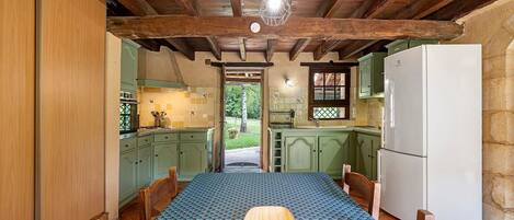 Una cocina rústica con vigas de madera, una mesa de comedor con mantel estampado y un refrigerador.