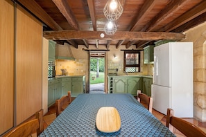 Una cocina rústica con vigas de madera, una mesa de comedor con mantel estampado y un refrigerador.