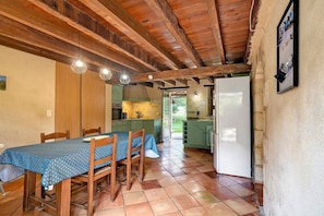 A dining area with a table set for four, wooden chairs, a kitchen with green cabinets, and a white refrigerator.