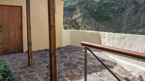 A stone-paved balcony with a wooden railing, a wooden door, and a view of a mountain with a structure on top. - Casa Rural Pepita - Gran Canaria Center - Tejeda (Pagos de Casas Juan Gómez)